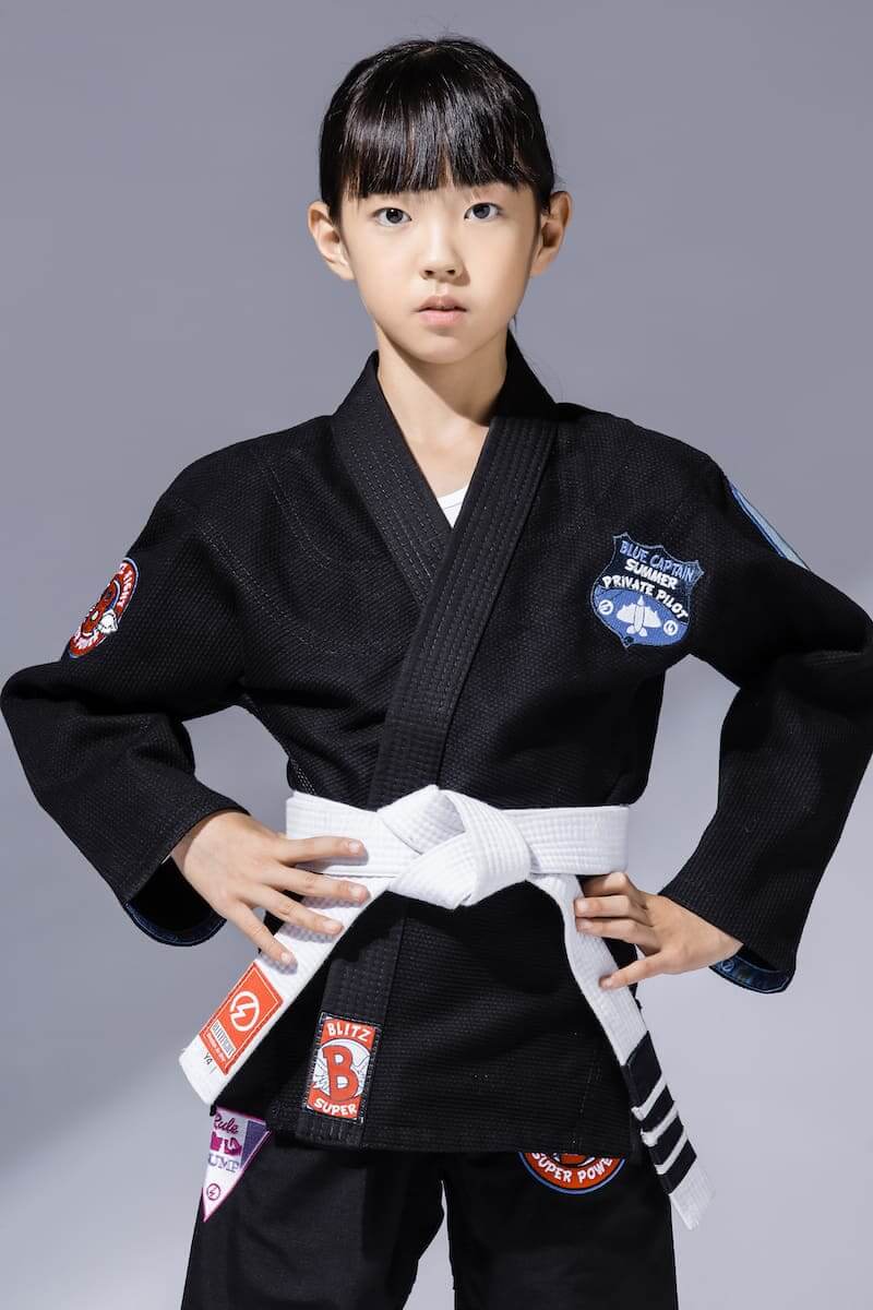 Girl wearing a kids jiu-jitsu gi in black with a white belt and patches for Brazilian Jiu-Jitsu training.