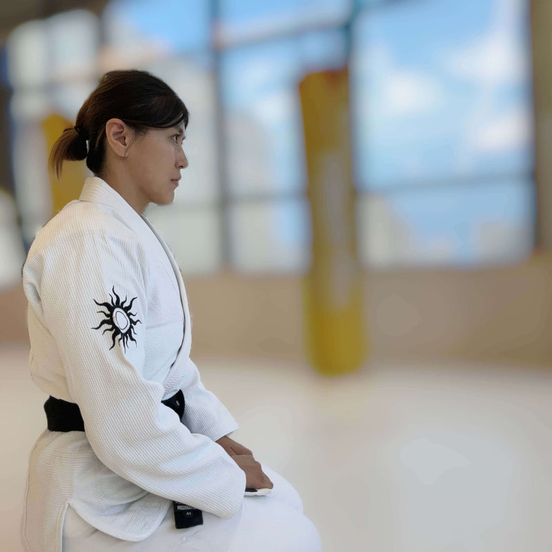 Female practitioner in premium BJJ Gi, focused and seated, showcasing distinct design elements of Signature BJJ Gi Collection.