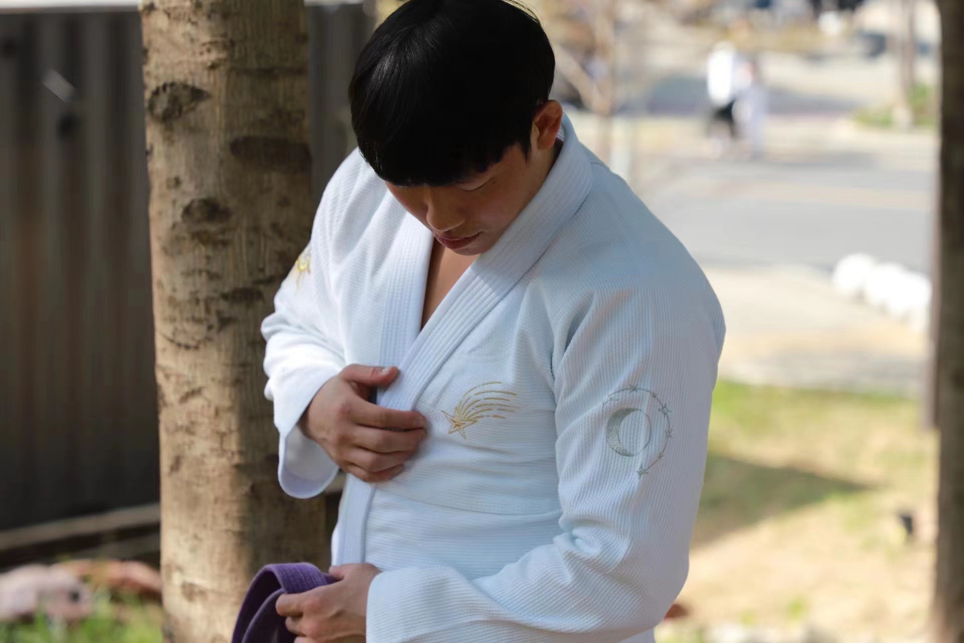 A person in a white bjj gi adjusting their uniform, showcasing detailed embroidery on their sleeve.