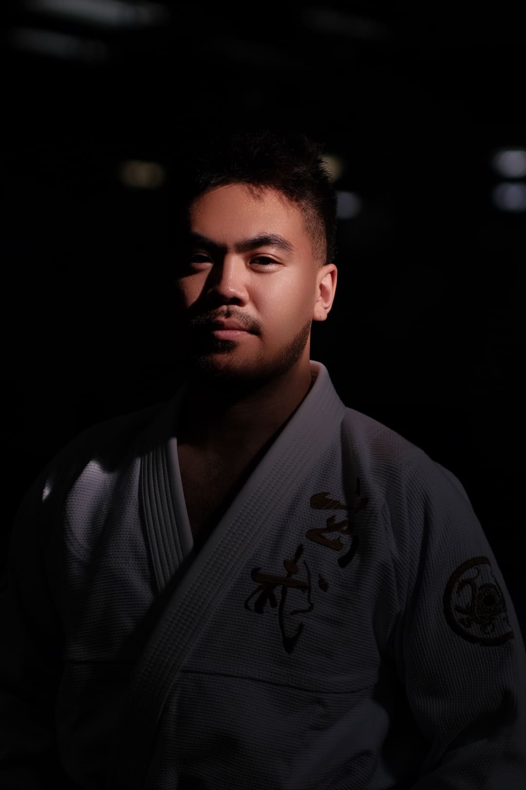 A person wearing a ZHAN Black Tortoise BJJ Gi stands in a dark setting, showcasing the gi's detail and design.