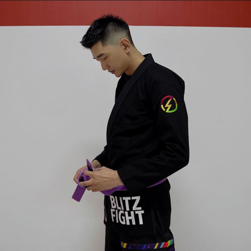 BLITZ DEFENSE Series Rainbow BJJ Set: Durable & Stylish Gi worn by a practitioner tying a purple belt.