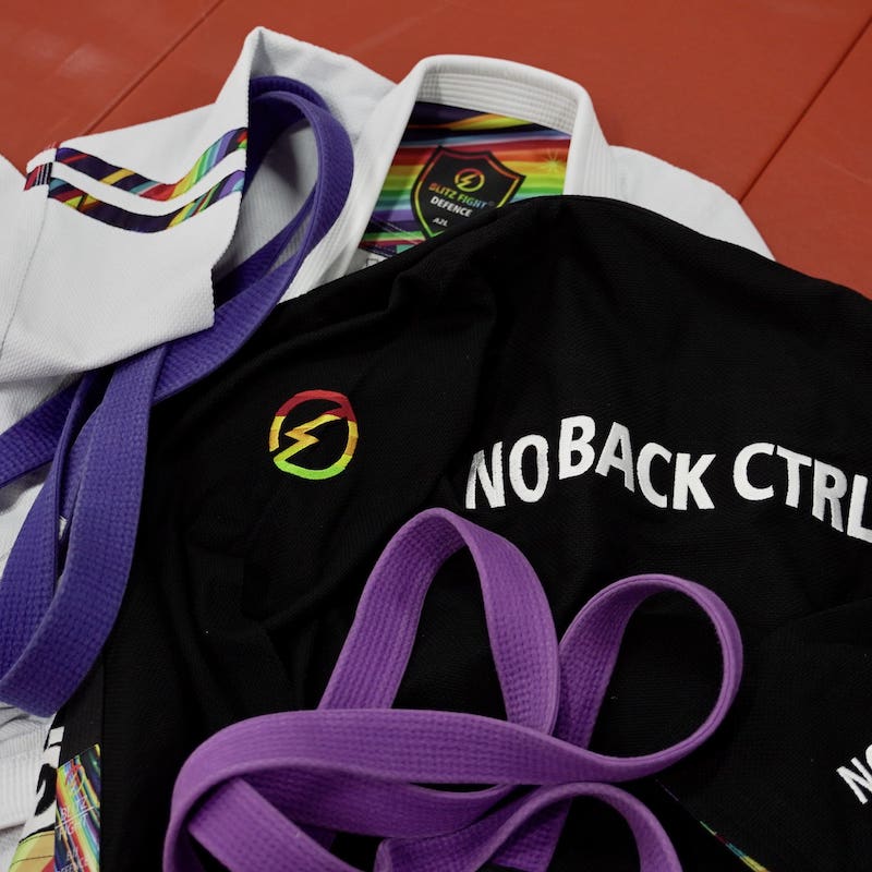 BLITZ DEFENSE Series Rainbow BJJ Set: Durable & Stylish Gi displayed with colorful belts on a training mat.