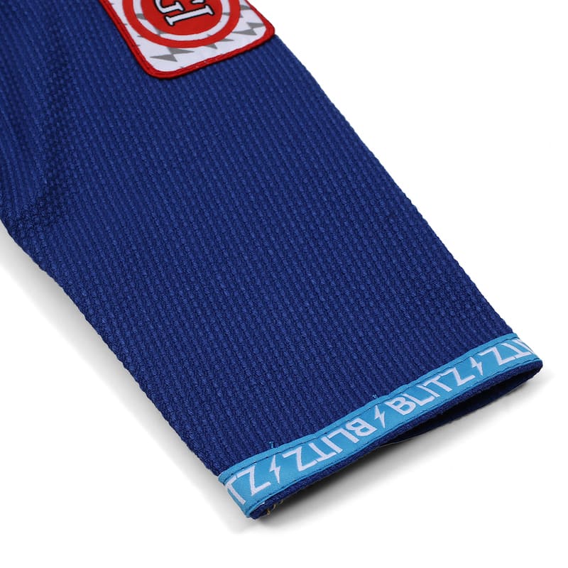 BLITZ Kids Classic BJJ Gi: Tradition & Excellence sleeve detail with embroidered logos and blue trim.