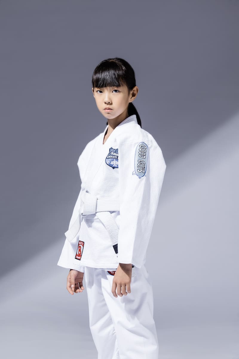 BLITZ Kids Super Power BJJ Gi worn by a young athlete posing confidently in a jiu-jitsu training environment.