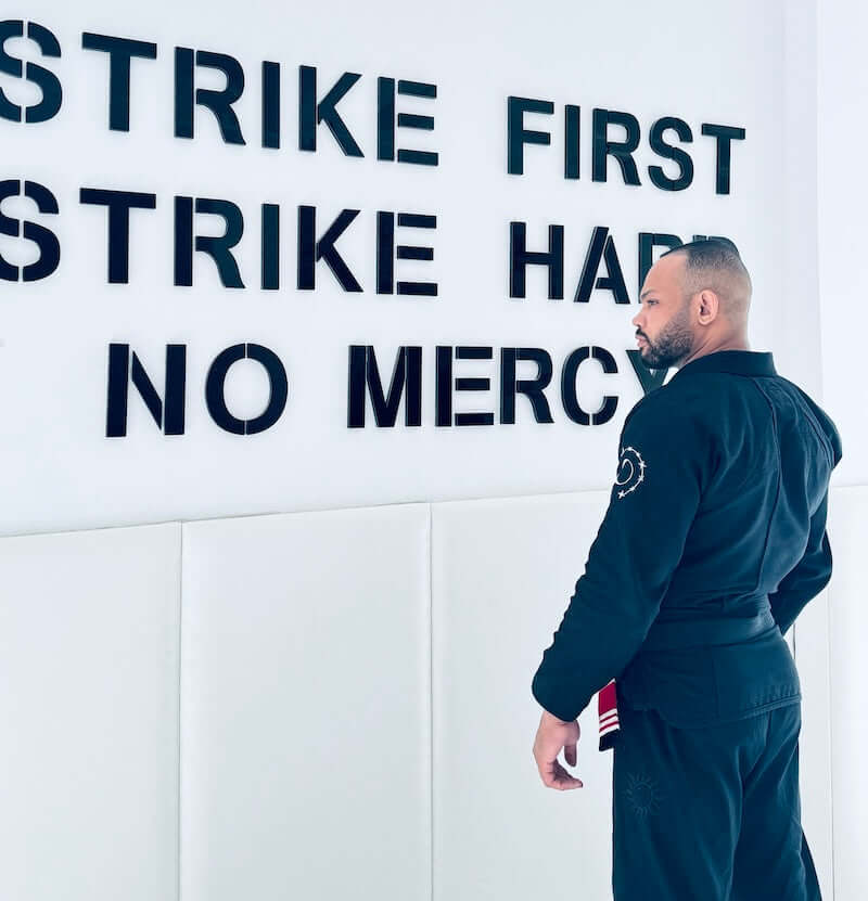 A practitioner wearing the BLITZ Sun & Moon Brazilian Jiu-Jitsu Gi stands in front of motivational wall text.