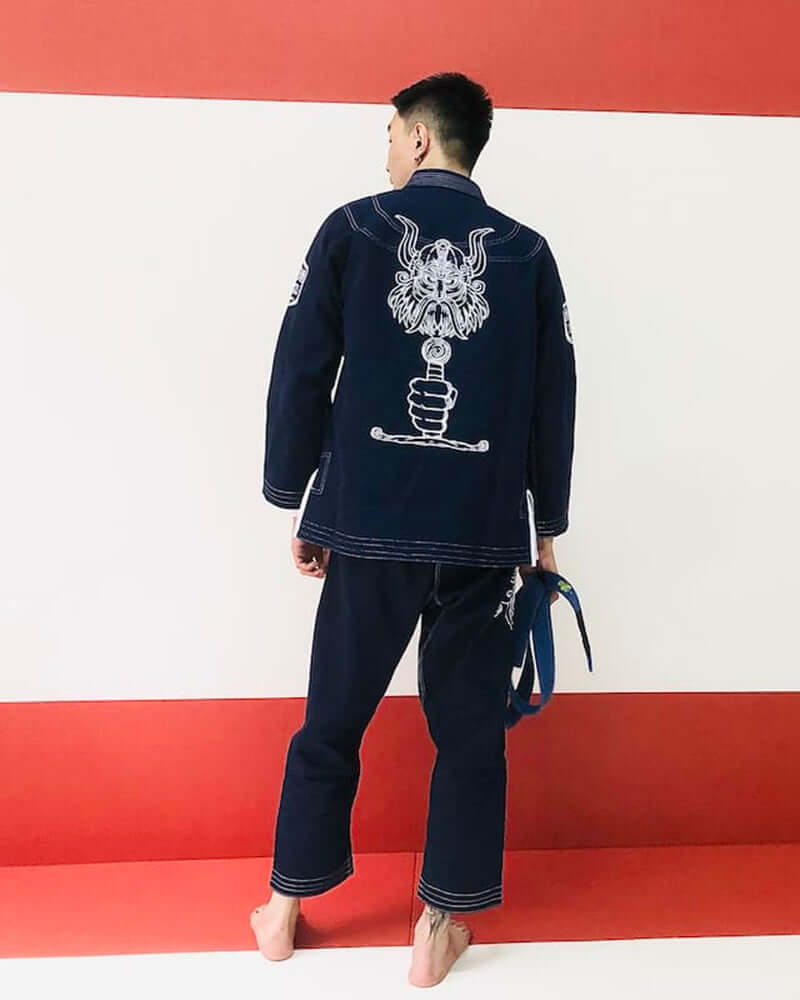A person wearing the BLITZ Viking God BJJ Gi, showcasing the Norse-inspired design on the back against a red backdrop.