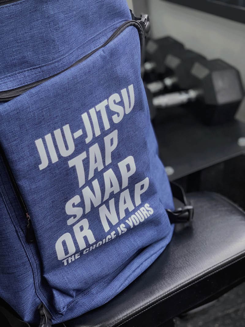 Ultimate BJJ Backpack: Spacious & Durable Gear Bag for Martial Artists on gym bench with weights in background.