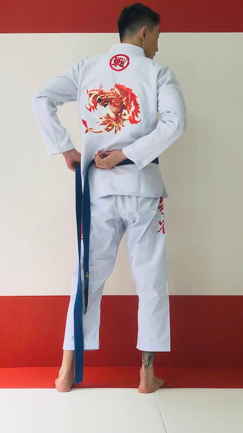 ZHAN Vermilion Phoenix BJJ Gi featuring phoenix artwork, embroidered details, and a practitioner tying a belt.