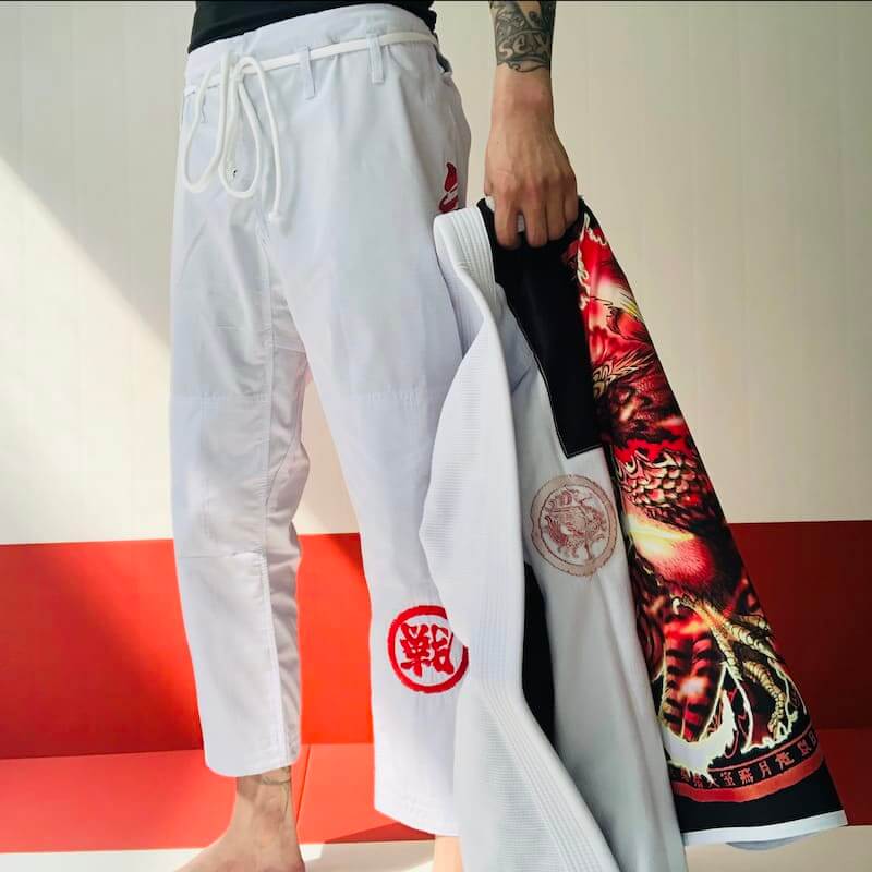 Person holding ZHAN Vermilion Phoenix BJJ Gi and pants, showcasing phoenix design and embroidered details.