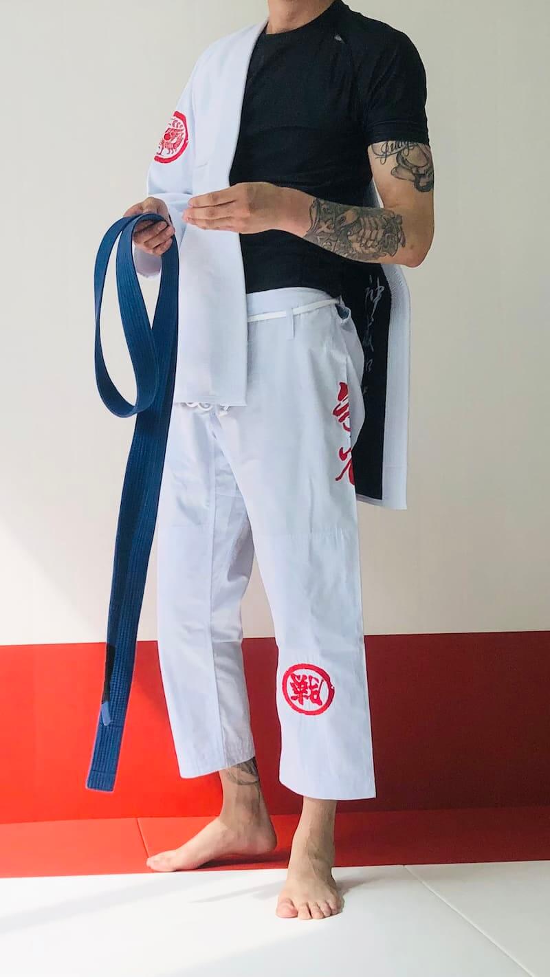 ZHAN Vermilion Phoenix BJJ Gi displayed on a practitioner holding a blue belt, showcasing its unique design and craftsmanship.