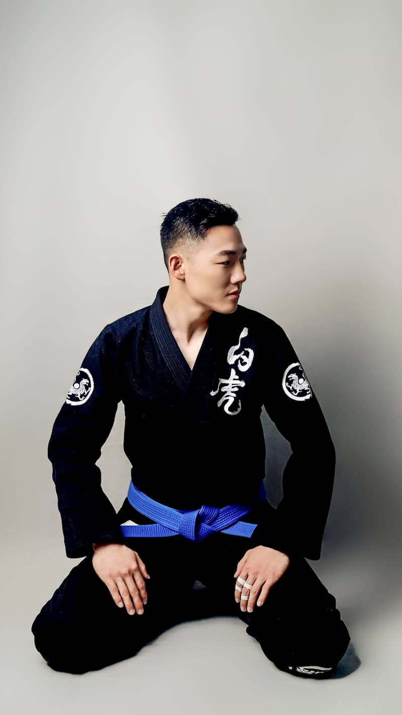 ZHAN White Tiger BJJ Gi worn by a martial artist in a kneeling pose with a blue belt.